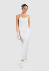 Vestido largo gris con tirantes finos, diseño ajustado y aberturas laterales. Combinado con zapatillas blancas, sobre un fondo liso.