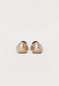 Zlaté metalické slip-on boty s texturovaným povrchem, zaoblenou špičkou a kontrastní béžovou gumovou podrážkou, zdobené minimálním šitím.