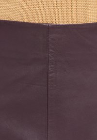 Burgundijas krāsas ādas svārki ar gludu tekstūru un redzamām šuvju detaļām, apvienoti ar gaiši dzeltenu adītu kreklu.