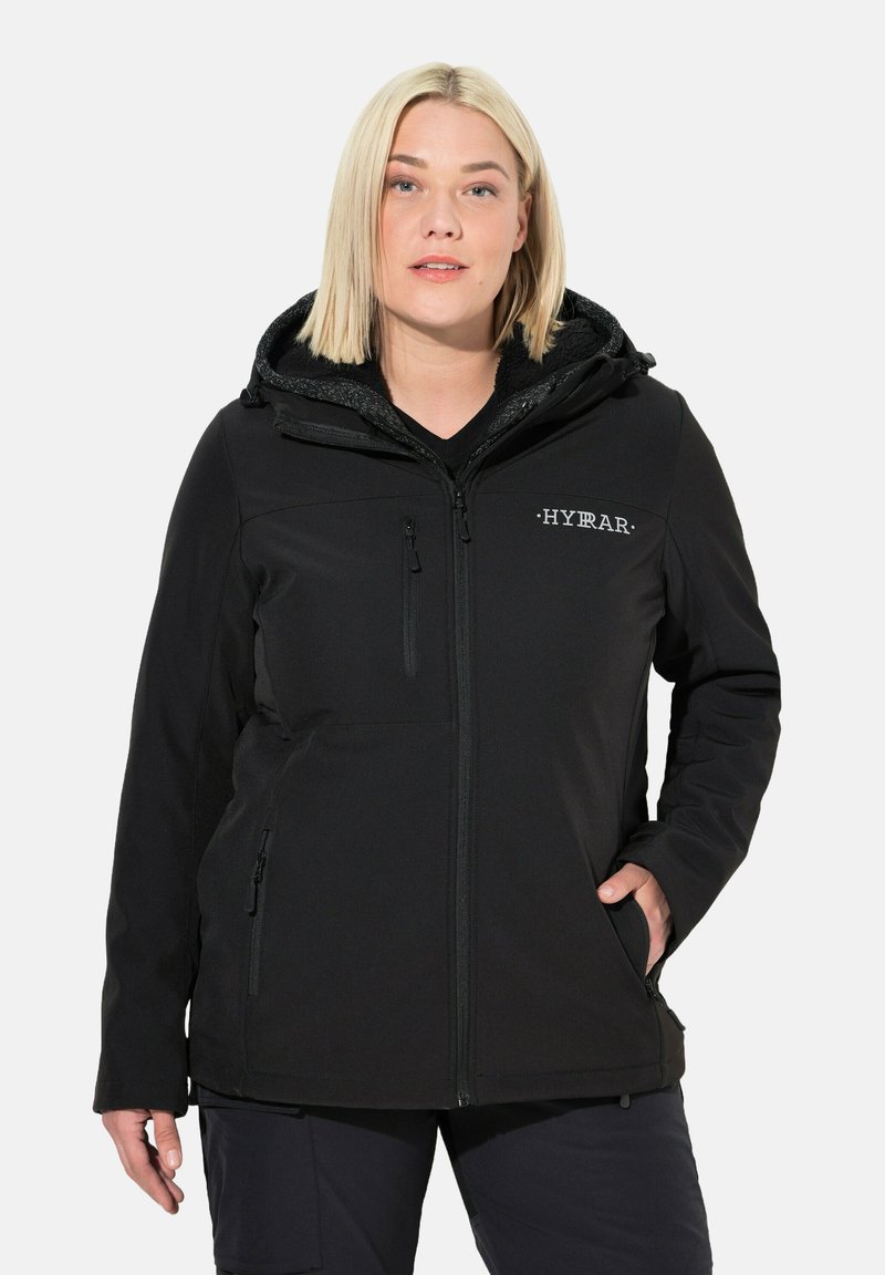Giacca softshell nera con cappuccio, dotata di una tasca sul petto con zip e tasche laterali. Il tessuto ha una texture liscia con un rivestimento in pile.