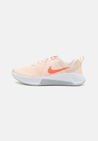 Lys ferskenfarvet sportssko med en tekstureret mesh-overdel, der har et iøjnefaldende orange swoosh-logo, hvid mellemsål og grå gummiydersål.