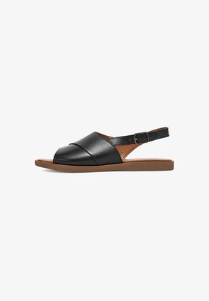 Sandalias slingback de cuero negro con punta redonda, diseño cruzado y suela plana color marrón claro. Incluyen correa ajustable en el tobillo.