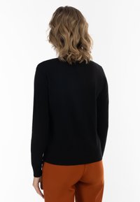 Maglione nero realizzato in materiale morbido, con maniche lunghe e scollatura rotonda. Indossato con pantaloni arancioni, che mostrano un design liscio e aderente.