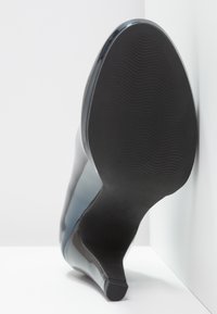 Tacchi in pelle verniciata nera con superficie liscia, punta arrotondata e suola in gomma dotata di scanalature orizzontali per una migliore trazione.