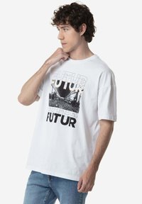 Camiseta de algodón blanca con un estampado gráfico que incluye la palabra "FUTUR" y una imagen en blanco y negro de una multitud. Manga corta y ajuste relajado.