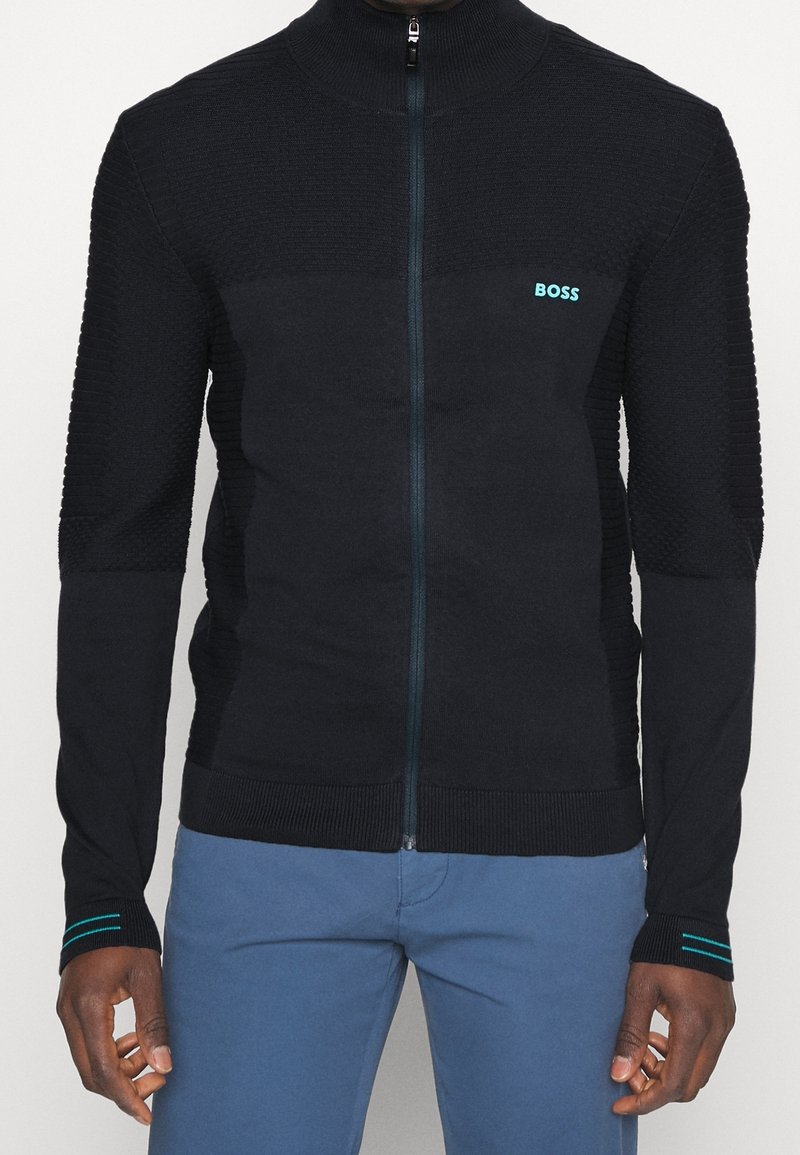 Svart zip-up tröja med texturerade axelpaneler, BOSS-logotyp i teal och ribbade mudd och nederkant. Slät tyg, skräddarsydd passform och subtila detaljer.
