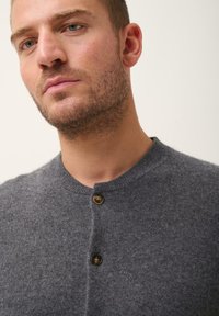 Šedý pletený cardigan s kulatým výstřihem, dvěma hnědými knoflíky a měkkou texturou. Zaměřte se na konzistenci látky a detail knoflíků.