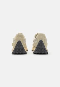 Ein Paar beigefarbene, strukturierte Sneakers, von hinten gezeigt, mit schwarzen, dreieckigen Sohlen, die kreisförmige Griffmuster auf einem weißen Hintergrund aufweisen.