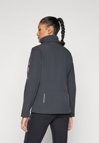 Black softshell jacket with a high collar, featuring a side pocket and contrasting pink logo detail on the upper arm. Smooth texture.