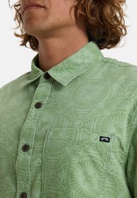 Lichtgroen shirt met een geometrisch patroon, voorzien van een knoopsluiting met een kraag, bruine knopen en een borstzak aan de linkerkant met een logo-label.
