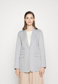 Blazer ajustado cinza claro com um único botão, dois bolsos e colarinho tipo lapela. Tecido fresco, forma estruturada e linhas limpas.
