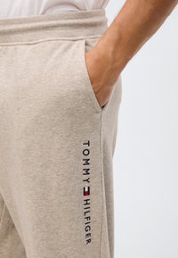 Beige sweatpants met een zachte textuur, voorzien van zijzakken en het "TOMMY HILFIGER" logo in marineblauw, naast een kleurdetail van de vlag.