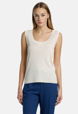 Light beige sleeveless top with a wide scoop neckline, made of a smooth, textured fabric, paired with blue tailored trousers.