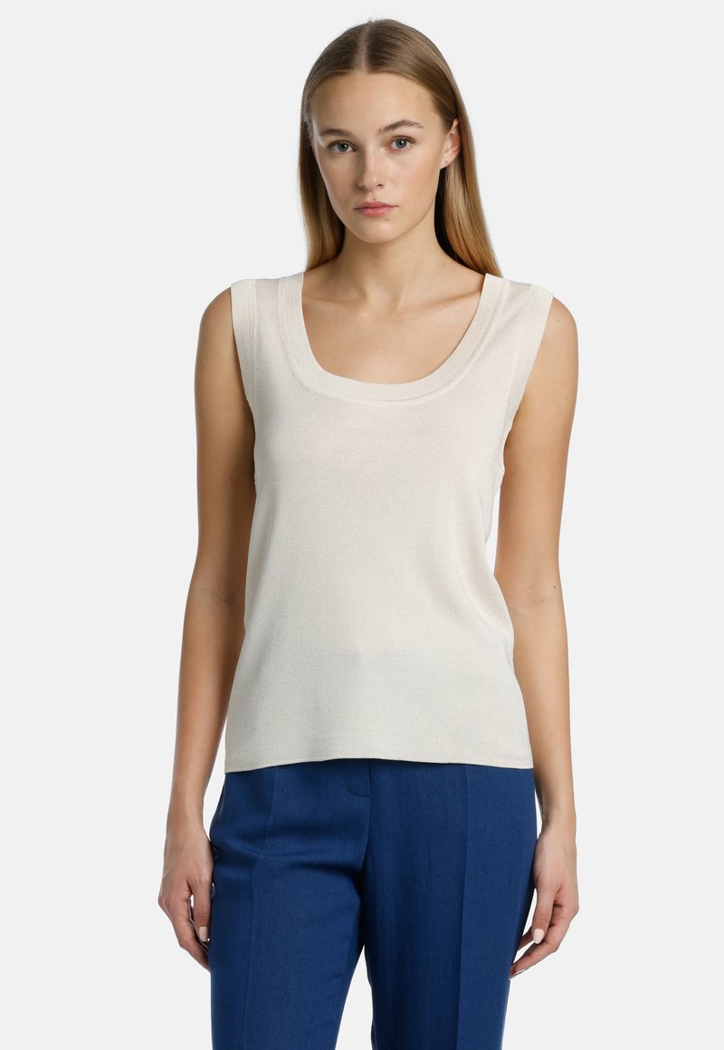 Top sin mangas de un beige claro con un escote amplio, hecho de una tela suave y texturizada, combinado con pantalones de corte recto en azul.