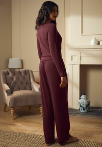 Conjunto de loungewear burdeos con top de manga larga y pantalones de pierna ancha, hecho de tela suave. Presenta una cinturilla elástica y cortes laterales.