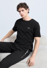 Μαύρο T-shirt με λευκό λογότυπο "BOSS" στο στήθος, σετ με μαύρο παντελόνι φόρμας που έχει γκρι ρίγα. Λείο ύφασμα και άνετη, καθημερινή εφαρμογή.