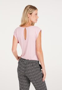 Top rosa a maniche corte con dettaglio a forma di chiave sul retro, abbinato a pantaloni a fantasia bianca e nera con vestibilità comoda e cintura elastica.