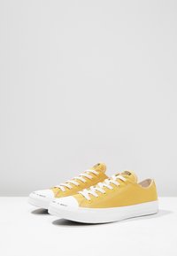 Baskets en toile jaune avec semelles et embouts en caoutchouc blanc, dotées de lacets blancs et d'un texte imprimé sur l'embout.