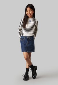 Camicia a maniche lunghe a righe beige e nera, abbinata a una gonna di jeans. Scarpe nere stringate e calzini neri completano l'outfit.