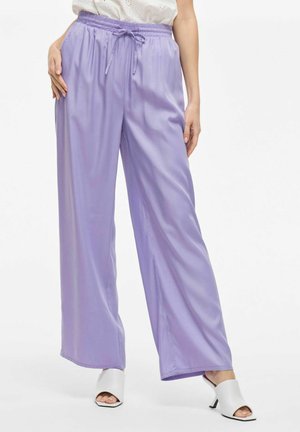 Lichtpaarse wijde broek met een elastische tailleband en trekkoorddetail, gemaakt van een gladde, glanzende stof, gecombineerd met witte open teen hakken.