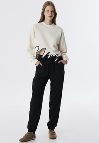 Sudadera color crema con cuello redondo, combinada con joggers negros que cuentan con cintura y puños elásticos, complementada con zapatos de ante marrones.