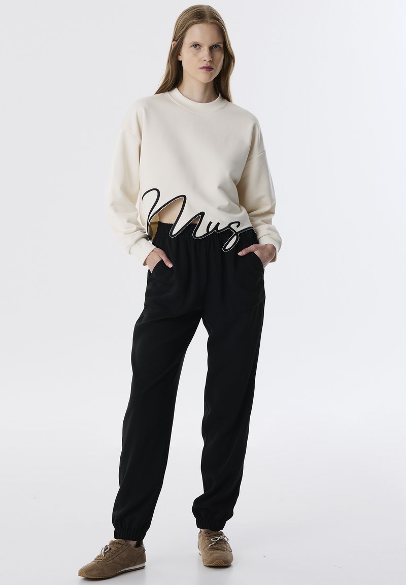 Sudadera color crema con cuello redondo, combinada con joggers negros que cuentan con cintura y puños elásticos, complementada con zapatos de ante marrones.