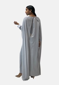 Lichtgrijze jurk met lange mouwen, een vloeiende cape-ontwerp, een afgeronde halslijn en een sleutelgatdetail aan de achterkant. Gladde, satijnachtige textuur.