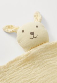 Mehka rumena otroška deka s pripetim glavico puhaste zajčke z vezenimi očmi, nosom, usti in visečimi uhlji na beli podlagi.