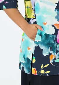 Kleurvolle tuniek met een bloemenontwerp in blauwe, groene en roze tinten, voorzien van een zijzak en een split aan de onderkant voor gemakkelijke beweging.