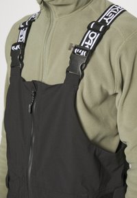 Black overalls with adjustable straps featuring a white graphic design. Zipper closure at the front, made from durable, textured material.