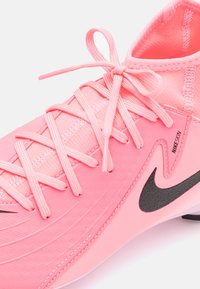 Roza atletska cipela s teksturiranim gornjim dijelom, ravnim vezicama i crnim Nike logom. Dizajn uključuje pojednostavljeni oblik i prozračan materijal.