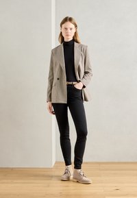 Checkered blazer with two pockets, black turtleneck, fitted black jeans, and beige lace-up ankle boots. Wooden floor, plain background.