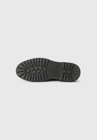 Suela de zapato de goma negra con surcos profundos, que presenta un logotipo circular y acentos texturizados para mayor agarre y durabilidad.