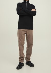 Col roulé en maille noire avec une fermeture éclair à l'avant, associé à un pantalon marron clair fuselé et des chaussures noires à lacets. Design simple et couleurs neutres.