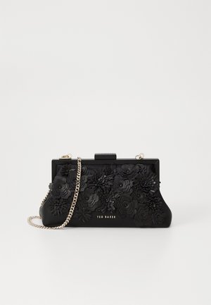 Czarna kopertówka z ozdobami kwiatowymi 3D, złotym łańcuszkiem i logo "Ted Baker" z przodu na białym tle.