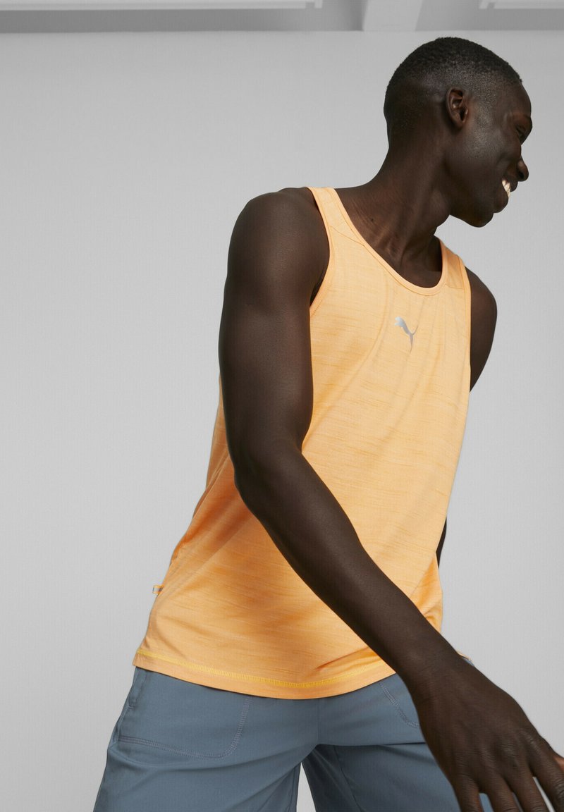 Débardeur de sport orange sans manches en tissu texturé, présentant un motif subtil, un col rond et un petit logo sur la poitrine.