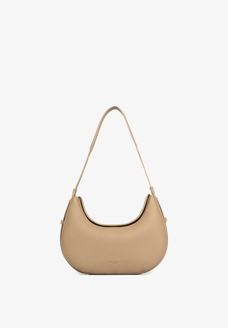 Sac à épaule en cuir beige texturé avec une forme courbée et une bandoulière unique suspendu sur un fond blanc.