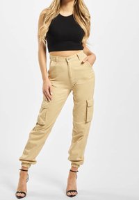 Khaki cargobroek met elastische boorden, meerdere zijzakken en een knoopsluiting. Gecombineerd met een zwart crop-top en sleehakken.