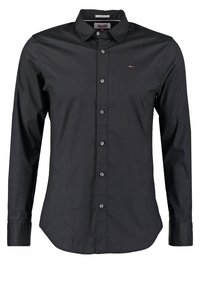 Camisa negra de manga larga con botones, fabricada en algodón y con cuello puntiagudo, que presenta un pequeño detalle de logo en el pecho y un corte regular.