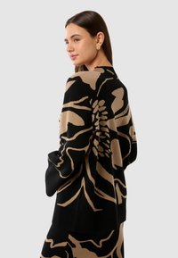 Maglione lavorato a maglia con grande motivo floreale nero e beige, vestibilità ampia, maniche lunghe e dettagli a coste lungo l'orlo e i polsini.