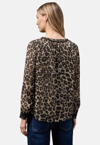 Bluse med leopardprint i transparent stof, der har rund halsudskæring, lange ærmer og smockede manchetter. Plisseret detalje bagpå tilføjer struktur.