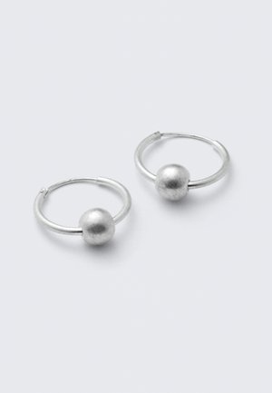 Paire de petites boucles d'oreilles créoles en argent, chacune avec une perle ronde en argent sur un fond gris clair.