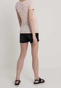 Ljusrosa och grårandig figursydd t-shirt, kombinerad med svarta shorts. Svarta sandaler med texturerad rem och kontrasterande vit sula.