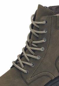 Brown leather ankle boot featuring rounded toe, thick sole, beige laces, and metal eyelets. Textured surface with stitching details.