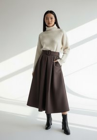 Brązowa plisowana spódnica z wysokim stanem i okrągłym paskiem, zestawiona z kremowym prążkowanym golfem i czarnymi botkami za kostkę.