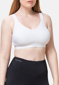 Reggiseno wireless bianco con superficie strutturata, spalline larghe e fascia liscia con il nome del marchio. Abbinato a leggings neri a vita alta.