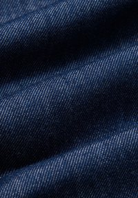 Ciemnoniebieska tkanina dżinsowa o gładkiej fakturze, z delikatnymi ukośnymi wzorami tkania i kontrastującymi jaśniejszymi nitkami.