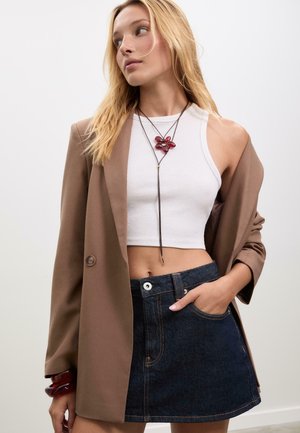 Hnedý blejzer cez biele crop top, skombinovaný s tmavými džínsovými sukňou. Obsahuje náhrdelník s červenou kvetinou a náramok na zápästí, a prednú kapsu.
