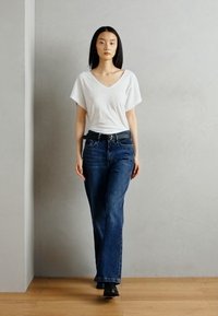 Witte v-hals t-shirt met brede mouwen, gecombineerd met donkerblauwe straight-leg jeans. Een zwarte riem en enkelboots maken de outfit compleet.