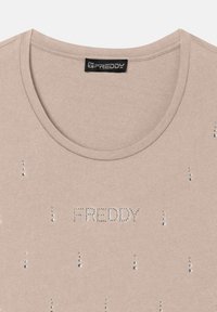 T-shirt in cotone beige con scollatura rotonda, decorato con piccoli strass trasparenti disposti intorno e che formano la scritta "FREDDY" al centro.